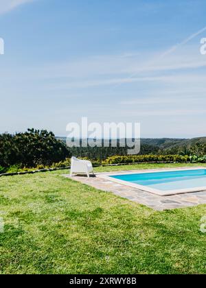 Un cadre serein au bord de la piscine avec des chaises longues blanches donnant sur une vue panoramique sur les montagnes luxuriantes sous un vaste ciel Banque D'Images