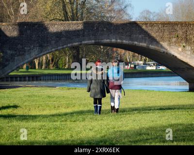 Abingdon prétend être la plus ancienne ville d'Angleterre. C'est son célèbre pont de pierre médiéval, vu par un beau matin d'été. Le pont a été commencé en 1416 et achevé en 1422, en utilisant du calcaire local. Ici, nous voyons un couple câlin marchant sur les rives de la Tamise vers le pont au lever du soleil. Banque D'Images