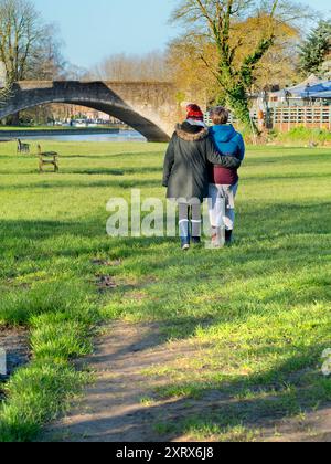 Abingdon prétend être la plus ancienne ville d'Angleterre. C'est son célèbre pont de pierre médiéval, vu par un beau matin d'été. Le pont a été commencé en 1416 et achevé en 1422, en utilisant du calcaire local. Ici, nous voyons un couple câlin marchant sur les rives de la Tamise vers le pont au lever du soleil. Banque D'Images