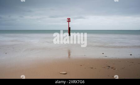 Un seul poste (groyne) dans la mer, à Swanage Beach, Dorset. les vagues chevauchent le poteau. Le jour est couvert et nuageux Banque D'Images