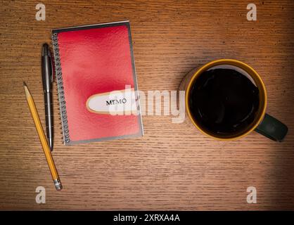 Café dans une tasse à bordure dorée sur une table en bois à côté d'un carnet de notes rouge et or avec stylo et crayon Banque D'Images