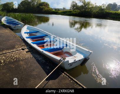 Fondé en 1921 et situé sur une belle partie de la Tamise dans l'Oxfordshire, Radley Boathouse sert Radley College et les amateurs d'aviron locaux depuis plus d'un siècle. Ici, nous voyons deux bateaux à rames amarrés par sa jetée, tôt par un beau matin d'été. Banque D'Images