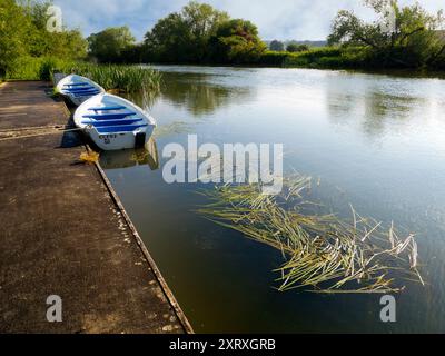 Fondé en 1921 et situé sur une belle partie de la Tamise dans l'Oxfordshire, Radley Boathouse sert Radley College et les amateurs d'aviron locaux depuis plus d'un siècle. Ici, nous voyons deux bateaux à rames amarrés par sa jetée, tôt par un beau matin d'été. Banque D'Images