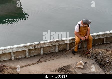 Fisherman organise des filets de pêche sur le bord de son bateau de pêche amarré dans le port après un voyage. Pêchez n'importe où. Banque D'Images