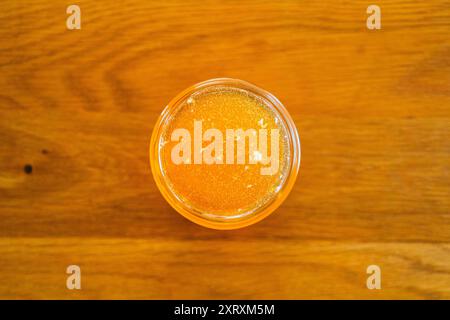 Vue de dessus de délicieux miel d'abeille dorée avec des bulles fraîchement récoltées debout sur une table en bois gros plan Banque D'Images