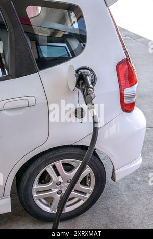 Plan vertical d'une buse de gaz dans le trou du réservoir d'essence d'une petite voiture blanche. Banque D'Images