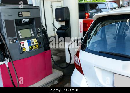 Gros plan horizontal d'une petite voiture blanche obtenant de l'essence à partir d'une buse à essence. Banque D'Images