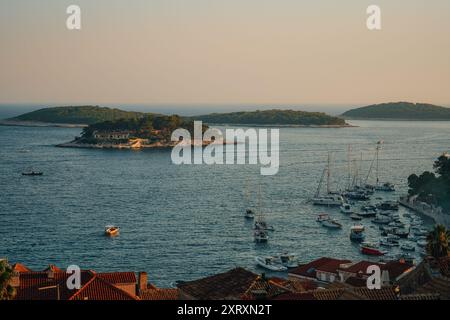 Une vue panoramique des bateaux amarrés près de la côte avec de petites îles en arrière-plan pendant le coucher du soleil à Hvar, Croatie. Banque D'Images