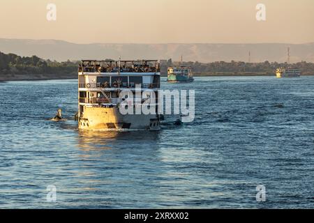 Louxor, Égypte ; 16 janvier 2024 : alors que le soleil plonge sous l'horizon lors d'une croisière sur le Nil de Louxor à Assouan. Les vendeurs locaux en petits bateaux naviguent à côté. Banque D'Images