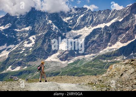 une femme randonneuse avec sac à dos et bâtons de randonnée s'arrête pour admirer l'impressionnant paysage montagneux des alpes sur le cervin sous un ciel bleu ensoleillé Banque D'Images