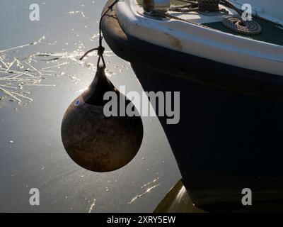 Bateau de plaisance et bouée amarrés sur la Tamise, le soleil se reflétant sur les eaux. Vu à Radley Boathouse ; construit en 1849, ce centre bien équipé pour l'aviron et les sports nautiques a la chance d'être situé sur un tronçon particulièrement beau de la Tamise. Mais voici la question : comment s'appelle la bouée ? Une petite recherche montre qu'il s'appelle différemment pare-chocs, garde-boue, boule de bateau, bouée d'amarrage, bouée d'ancre et probablement plusieurs autres noms que j'ai manqués. Mais nous soucions-nous vraiment, de toute façon ? Banque D'Images