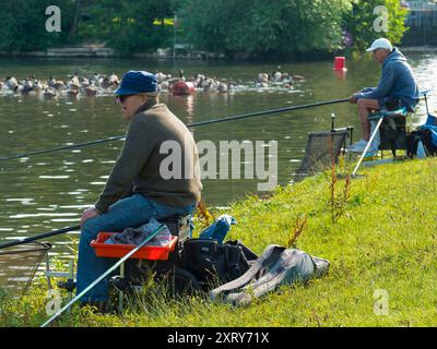 Des pêcheurs et un troupeau de Canadagais sur la Tamise à Abingdon, juste à côté de l'écluse d'Abingdon et de Weir. Branta canadensis est originaire des régions arctiques et tempérées de l'Amérique du Nord et a été introduit avec succès au Royaume-Uni. Il peut maintenant être vu à peu près n'importe où autour de la Tamise. Les pêcheurs sont intéressés par les poissons, pas les oiseaux, cependant... Banque D'Images