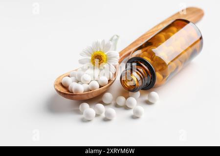 Remède homéopathique. Cuillère avec des pilules, bouteille et fleur de camomille sur fond blanc Banque D'Images