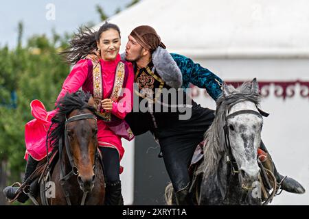 Homme nomade sur son cheval essayant d'embrasser la femme en tenue locale sur son cheval, dans le cadre de jeux nomades, à Almaty, Kazakhstan. Banque D'Images