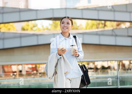 Jeune femme appréciant le café du matin tout en marchant dans la zone urbaine Banque D'Images