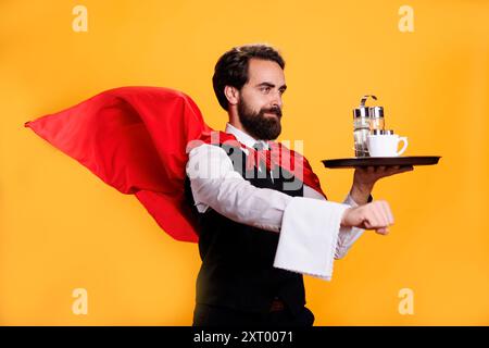 Maître d'hôtel de personnage héros tenant la plaque et portant le manteau sur fond jaune, personne travaillant comme serveur de restaurant de luxe. Super-héros servant de la nourriture sur plateau dans le studio, ouvrier de la gastronomie. Banque D'Images