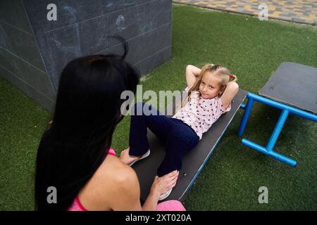 Mère et fille se livrant à des activités de conditionnement physique dans une aire de jeux par une journée ensoleillée Banque D'Images