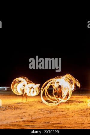 Les artistes du feu effectuent des manœuvres spectaculaires et palpitantes, respirent le feu et mangent les flammes, devant les spectateurs sur la plage. Tourbillonnement, lancer et sp Banque D'Images