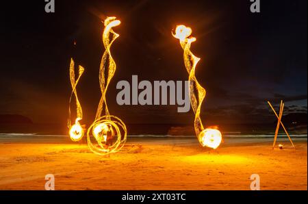 Les artistes du feu effectuent des manœuvres spectaculaires et palpitantes, respirent le feu et mangent les flammes, devant les spectateurs sur la plage. Tourbillonnement, lancer et sp Banque D'Images