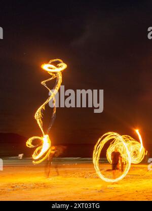 Les artistes du feu effectuent des manœuvres spectaculaires et palpitantes, respirent le feu et mangent les flammes, devant les spectateurs sur la plage. Tourbillonnement, lancer et sp Banque D'Images