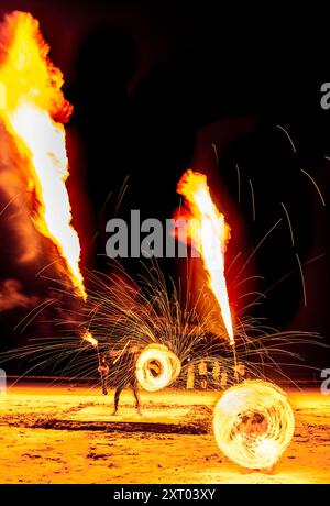 Les artistes du feu effectuent des manœuvres spectaculaires et palpitantes, respirent le feu et mangent les flammes, devant les spectateurs sur la plage. Tourbillonnement, lancer et sp Banque D'Images