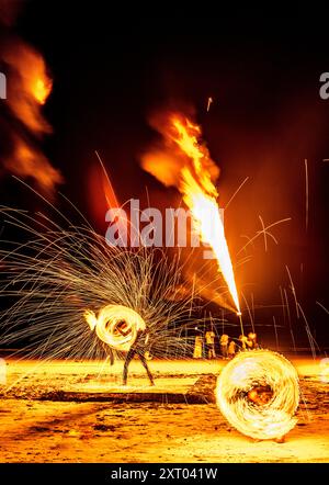 Les artistes du feu effectuent des manœuvres spectaculaires et palpitantes, respirent le feu et mangent les flammes, devant les spectateurs sur la plage. Tourbillonnement, lancer et sp Banque D'Images