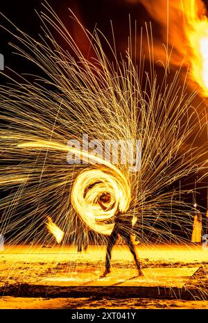 Les artistes du feu effectuent des manœuvres spectaculaires et palpitantes, respirent le feu et mangent les flammes, devant les spectateurs sur la plage. Tourbillonnement, lancer et sp Banque D'Images