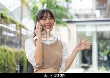 Une belle femme asiatique confiante parle au téléphone avec quelqu'un tout en se tenant dehors. personnes et concepts de technologie sans fil Banque D'Images