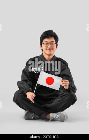 Jeune officier de police asiatique avec drapeau du Japon assis sur fond clair Banque D'Images