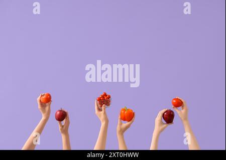 Mains avec tomates fraîches, pommes et poivrons sur fond lilas Banque D'Images