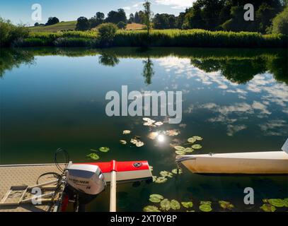 Fondé en 1921 et situé sur une belle partie de la Tamise dans l'Oxfordshire, Radley Boathouse sert Radley College et les amateurs d'aviron locaux depuis plus d'un siècle. Si vous vous tenez sur sa jetée et regardez à travers la rive nord de la rivière, vous verrez un arbre isolé et plutôt charmant, qui semble changer de caractère et d'apparence tout au long de l'année. Ici, nous le voyons par une belle et ensoleillée matinée d'été, avec les catamarans de plaisir omniprésents du hangar à bateaux au premier plan. La Croix de Malte rouge est l'emblème du club de navigation de l'université. Banque D'Images
