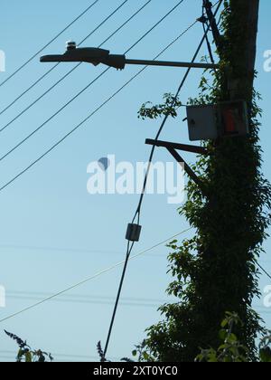 Je me promène dans mon village natal de Radley tous les jours, et je porte toujours un appareil photo. C'est surprenant ce que vous voyez parfois, même lors de promenades que vous avez faites des centaines de fois et que vous pensez savoir à l'envers. Ici, nous voyons un poteau portant un lampadaire, des fils téléphoniques et des câbles assortis sur ma promenade à travers Lower Radley jusqu'à la Tamise, avec une montgolfière flottant sereinement au-dessus. Banque D'Images