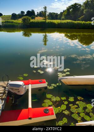 Fondé en 1921 et situé sur une belle partie de la Tamise dans l'Oxfordshire, Radley Boathouse sert Radley College et les amateurs d'aviron locaux depuis plus d'un siècle. Si vous vous tenez sur sa jetée et regardez à travers la rive nord de la rivière, vous verrez un arbre isolé et plutôt charmant, qui semble changer de caractère et d'apparence tout au long de l'année. Ici, nous le voyons par une belle et ensoleillée matinée d'été, avec les catamarans de plaisir omniprésents du hangar à bateaux au premier plan. La Croix de Malte rouge est l'emblème du club de navigation de l'université. Banque D'Images