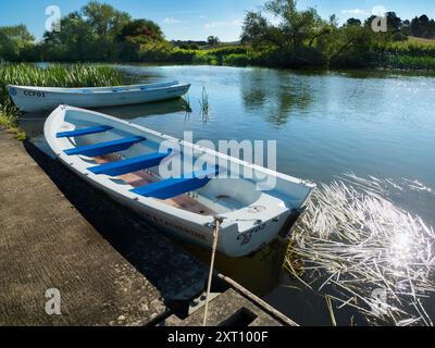 Fondé en 1921 et situé sur une belle partie de la Tamise dans l'Oxfordshire, Radley Boathouse sert Radley College et les amateurs d'aviron locaux depuis plus d'un siècle. Ici, nous voyons deux bateaux à rames amarrés par sa jetée, tôt par un beau matin d'été. Banque D'Images