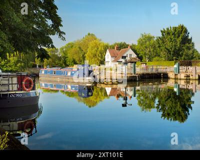 La zone autour de Sandford Lock Over the Thames est un endroit très apprécié des joggeurs, promeneurs, amateurs de chiens et beaucoup de gens fréquentant les grandes promenades dans cette région. Un nouveau boulanger artisanal proposant du pain au levain à la pointe est désormais une attraction locale... Ici, nous voyons des péniches amarrées par l'écluse, avec la maison d'écluse en arrière-plan, tôt un beau matin d'été. Je suis en route pour ramasser le pain. C'est le petit déjeuner trié, alors ! Banque D'Images