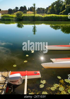 Fondé en 1921 et situé sur une belle partie de la Tamise dans l'Oxfordshire, Radley Boathouse sert Radley College et les amateurs d'aviron locaux depuis plus d'un siècle. Si vous vous tenez sur sa jetée et regardez à travers la rive nord de la rivière, vous verrez un arbre isolé et plutôt charmant, qui semble changer de caractère et d'apparence tout au long de l'année. Ici, nous le voyons par une belle et ensoleillée matinée d'été, avec les catamarans de plaisir omniprésents du hangar à bateaux au premier plan. La Croix de Malte rouge est l'emblème du club de navigation de l'université. Banque D'Images