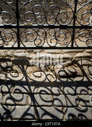 Ici, nous voyons la porte en fer forgé à l'entrée principale d'une maison dans West St Helens Street, l'une des plus anciennes parties d'Abingdon dans l'Oxfordshire. Elle tire son nom de l'église anglo-saxonne à une extrémité. Ici, à la première lumière, les garde-corps de la porte jettent des ombres intrigantes sur l'allée pavée. Banque D'Images