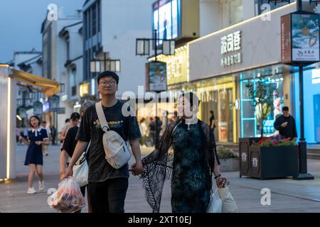 Suzhou, Chine - 11 juin 2024 : Un jeune couple marche main dans la main dans une rue animée de Suzhou, Chine. Banque D'Images