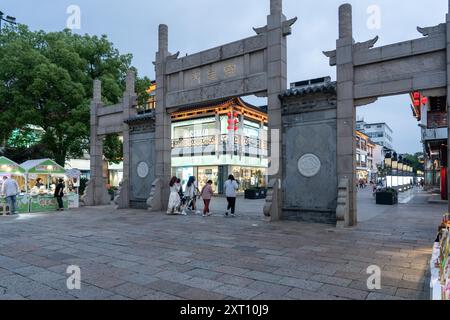 Suzhou, Chine - 11 juin 2024 : Une arche en pierre à Suzhou, Chine, mène à une rue avec des magasins et des vendeurs. Banque D'Images