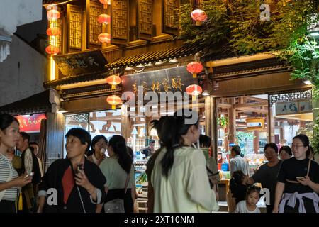 Suzhou, Chine - 11 juin 2024 : Une rue bondée à Suzhou, Chine la nuit, avec des lanternes rouges suspendues au-dessus d'une entrée de magasin. Banque D'Images
