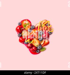 Divers fruits et légumes colorés forment une forme de cœur, symbolisant une alimentation saine et l'amour pour les aliments nutritifs, sur un fond rose. Banque D'Images