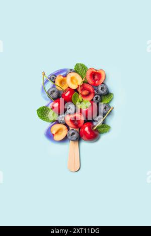 Cerises fraîches, bleuets et tranches de banane et de pêche présentées habilement sur un bâton de popsicle sur un fond bleu doux. Banque D'Images