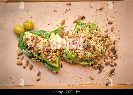 Vue de dessus de deux toasts à l'avocat surmontés de graines et d'olives, disposés sur du papier brun, offrant une option de petit déjeuner saine et nutritive Banque D'Images