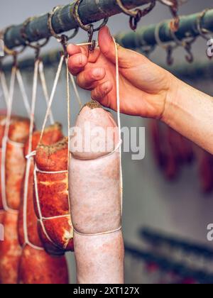 Une vue rapprochée des mains d’une personne attachant soigneusement de la ficelle autour des saucisses sobrasada suspendues dans une installation de salaison de viande traditionnelle. Banque D'Images