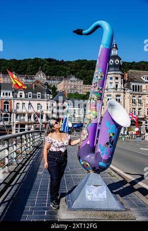 Dinant, Namur, Wallonie, Belgique. Juin 6, 2024.touriste féminine debout sur le pont regardant vers le haut admirant la sculpture de saxophone violet, portant un décolleté bas, Banque D'Images