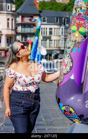 Dinant, Namur, Wallonie, Belgique. 6 juin 2024. Touriste adulte regardant vers le haut admirant la sculpture violette colorée, portant un décolleté bas, bâtiments sur Banque D'Images