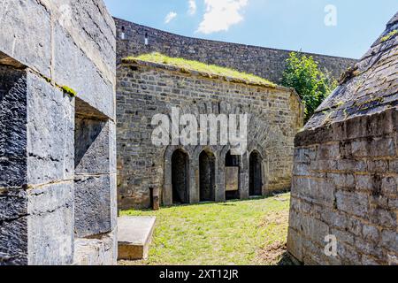 Passage extérieur entre les bâtiments épais aux murs de pierre de la forteresse Charlemont, petites portes voûtées en arrière-plan, pelouse verte clairsemée, ensoleillé d été Banque D'Images