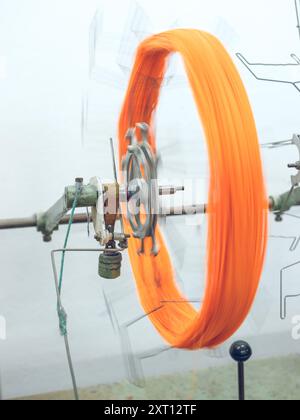 Un fil orange vif filant rapidement sur les machines dans une usine textile, transmettant un sens du mouvement dans le processus de production Banque D'Images