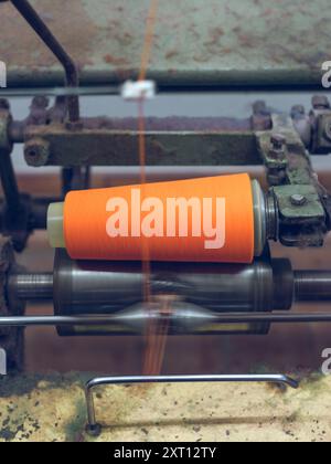 Gros plan d'un fil orange vif filé sur des machines industrielles dans une usine de fabrication de textile, avec un effet de mouvement flou Banque D'Images