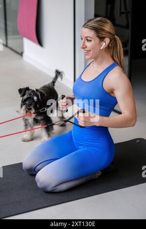 Une femme optimiste aime sa formation de bande de résistance dans le gymnase, accompagnée de son chien de compagnie enthousiaste Banque D'Images